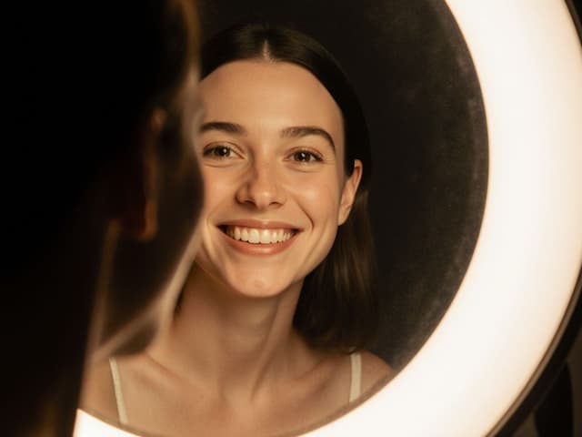 Person smiling genuinely at their reflection representing self-compassion and positive mirror work